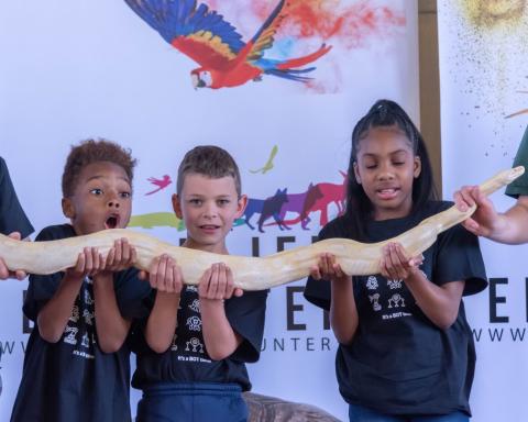 Three excited children hold a snake at an animal program