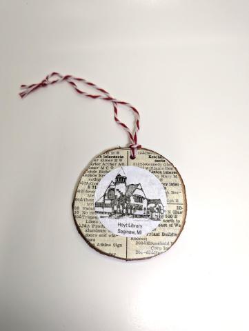 Hoyt Library line drawing image on a wood slice ornament with book page background