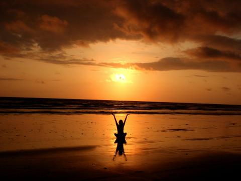 photo of person sitting on the beach with orange sunset in background