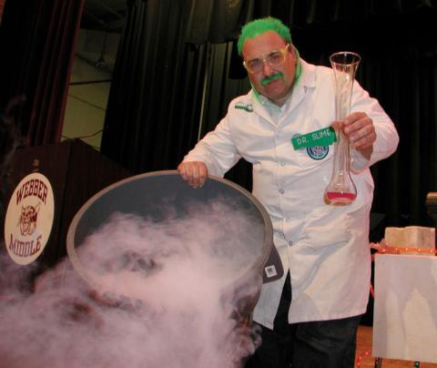 Dr. Slime, with green hair and mustache and a lab coat, is shown doing a science experiment.