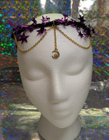 A crown on a mannequin head made of pipe cleaners, purple star tinsel with a charm focal in front suspended by chain.
