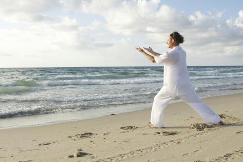 man doing tai chi moves on a beach with blue sky