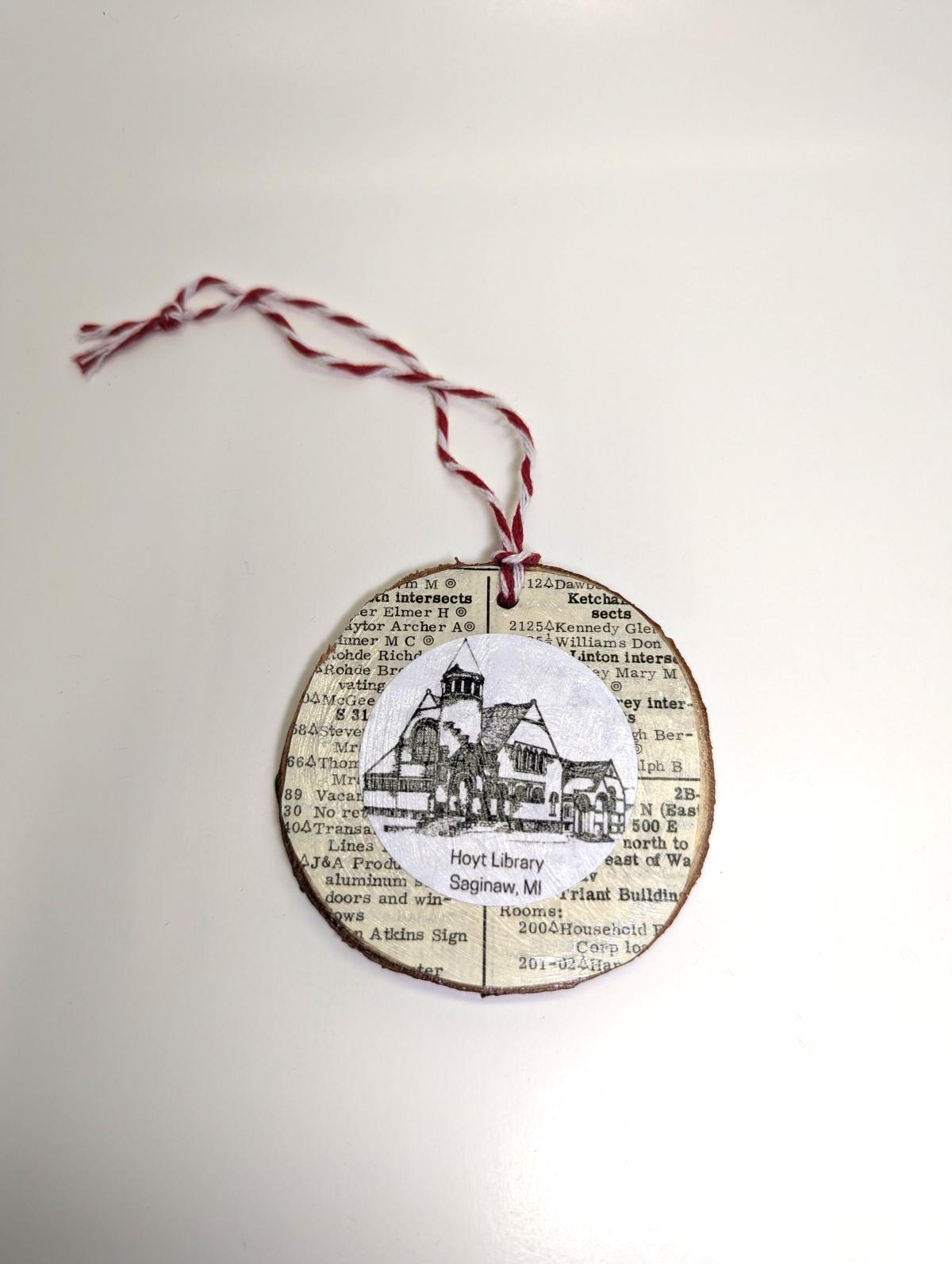 Hoyt Library line drawing image on a wood slice ornament with book page background