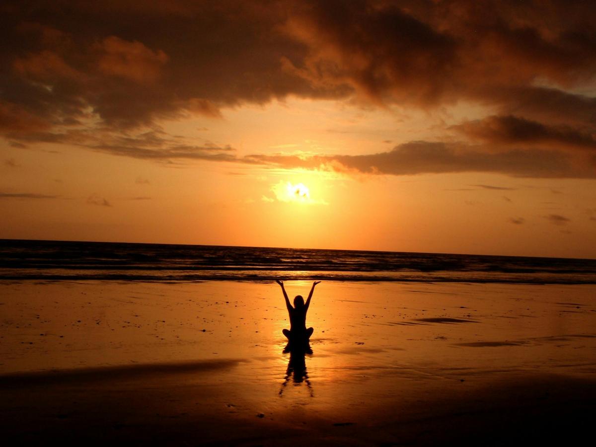 photo of person sitting on the beach with orange sunset in background