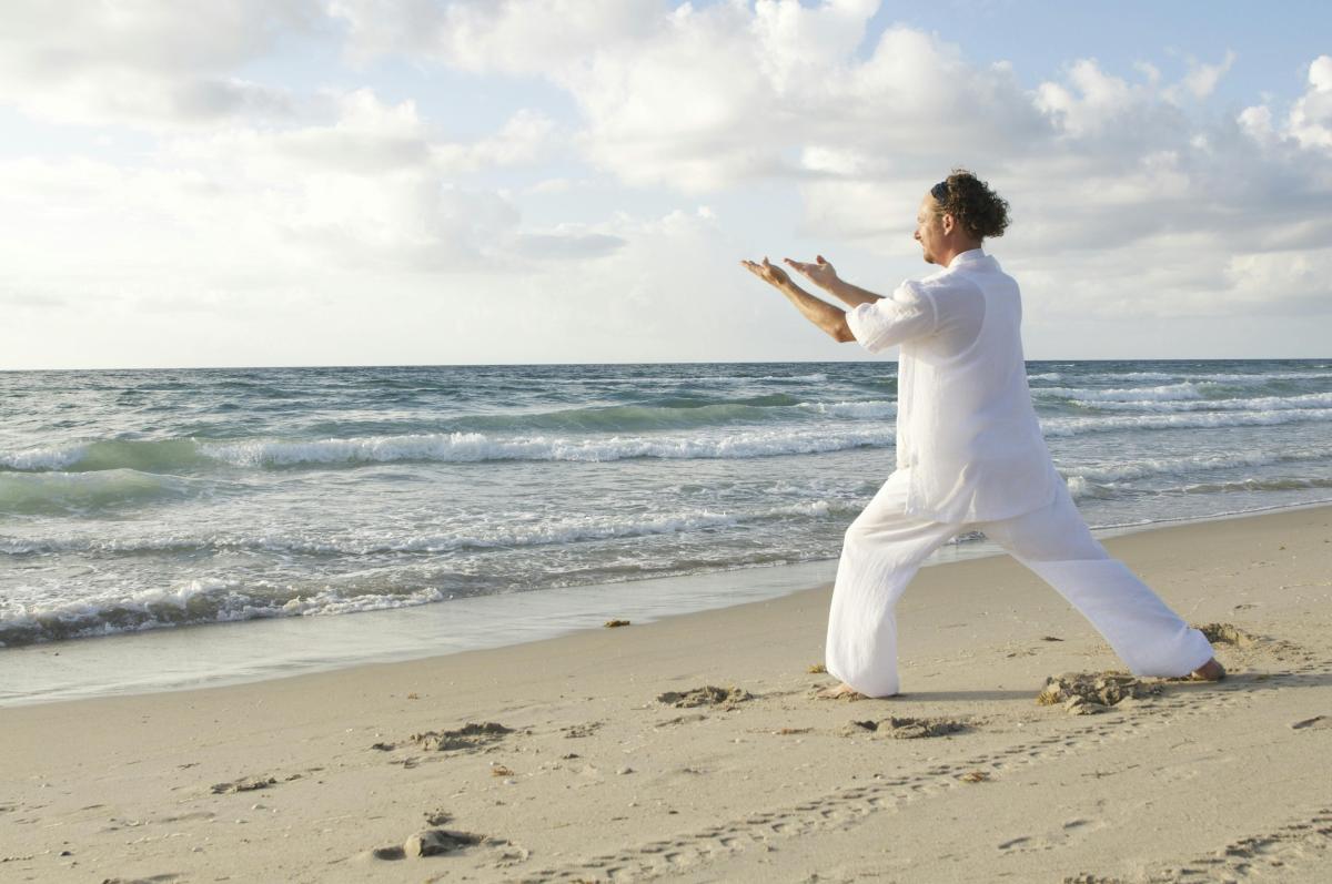 man doing tai chi moves on a beach with blue sky